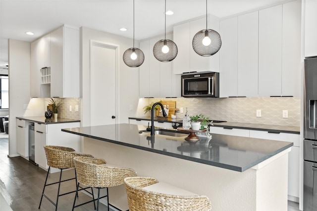 kitchen featuring an island with sink, sink, pendant lighting, and white cabinets