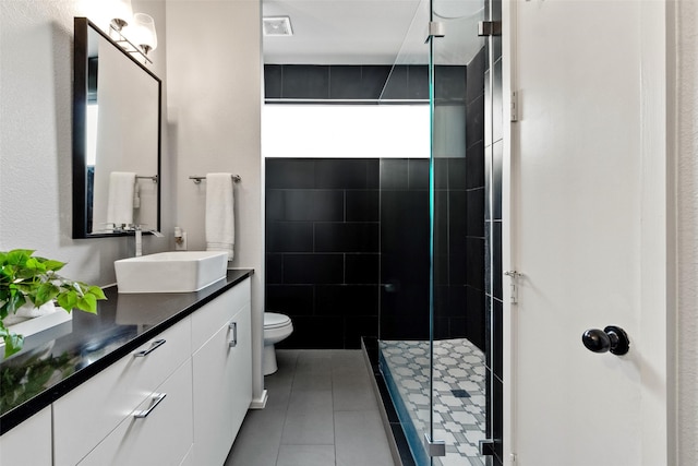 bathroom with a shower with door, vanity, tile patterned floors, and toilet