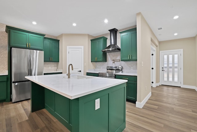 kitchen with an island with sink, sink, stainless steel appliances, light stone countertops, and wall chimney exhaust hood