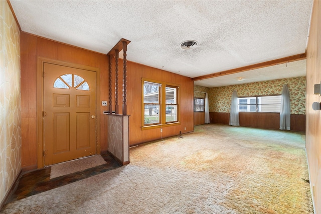 foyer featuring carpet, wooden walls, and a textured ceiling