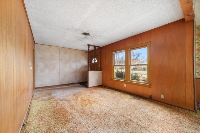 carpeted empty room featuring wooden walls and a textured ceiling