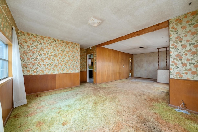 carpeted empty room with wooden walls and a textured ceiling