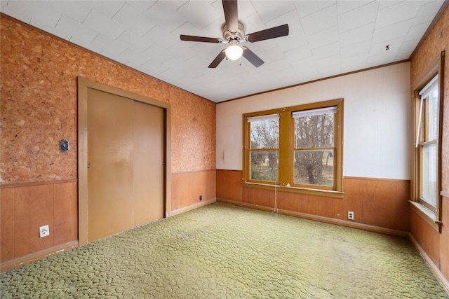 carpeted spare room featuring crown molding, ceiling fan, and wooden walls