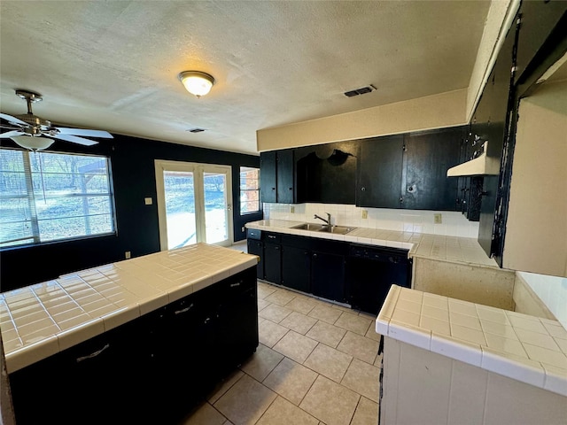 kitchen with black dishwasher, sink, decorative backsplash, tile counters, and a textured ceiling