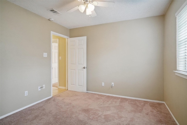 empty room with ceiling fan, light colored carpet, and a textured ceiling