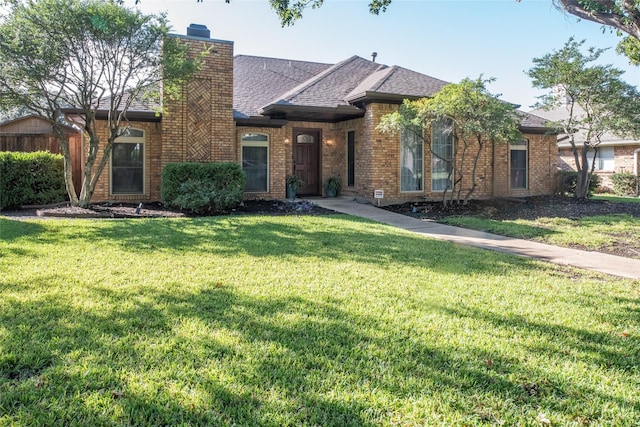 view of front of home with roof with shingles, a front lawn, a chimney, and brick siding