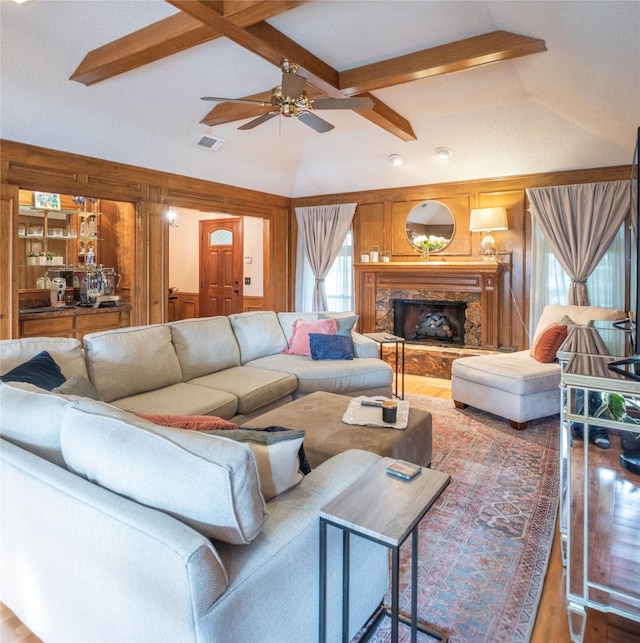 living room with wood walls, lofted ceiling with beams, hardwood / wood-style flooring, ceiling fan, and a high end fireplace