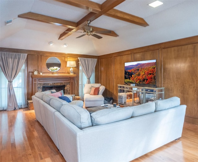 living room with vaulted ceiling with beams, light wood-type flooring, wooden walls, ceiling fan, and a premium fireplace