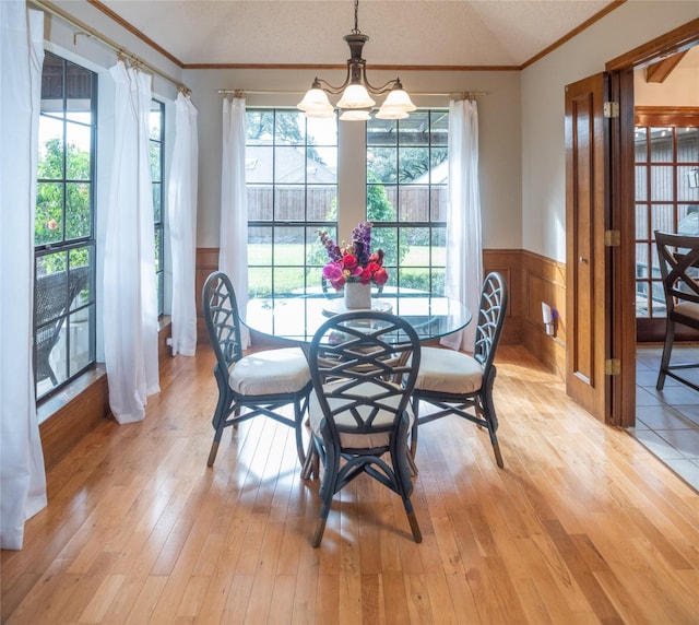 dining area with lofted ceiling, a notable chandelier, ornamental molding, light hardwood / wood-style floors, and a textured ceiling