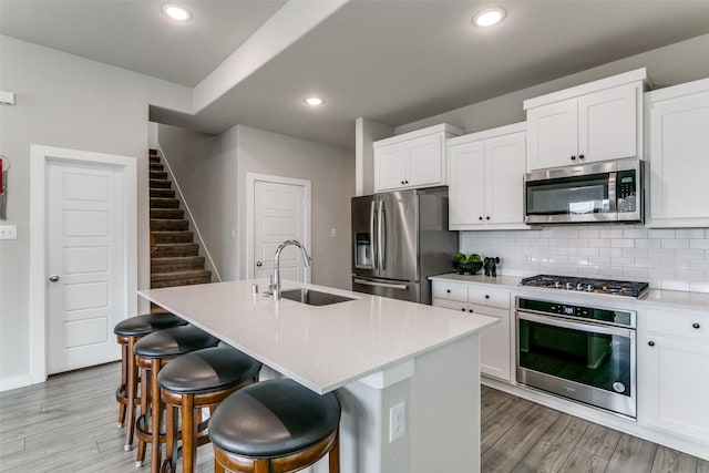 kitchen with white cabinetry, appliances with stainless steel finishes, a kitchen island with sink, and sink