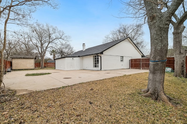 view of side of home featuring an outbuilding, a fenced backyard, a chimney, and a patio