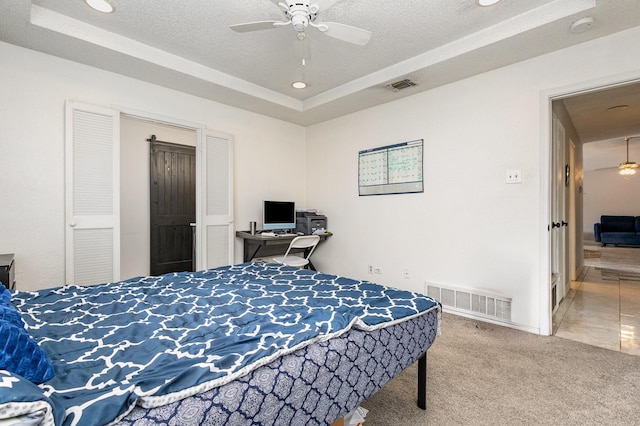 carpeted bedroom featuring ceiling fan, a raised ceiling, and a textured ceiling