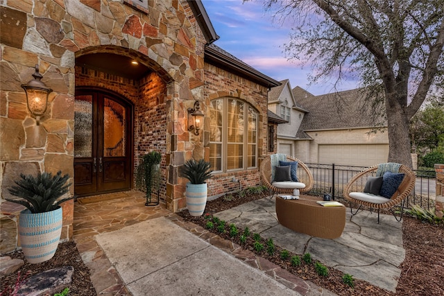 exterior entry at dusk with a garage, stone siding, brick siding, and french doors