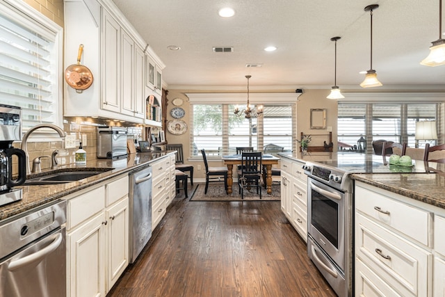 kitchen with sink, decorative light fixtures, dark stone counters, stainless steel appliances, and white cabinets