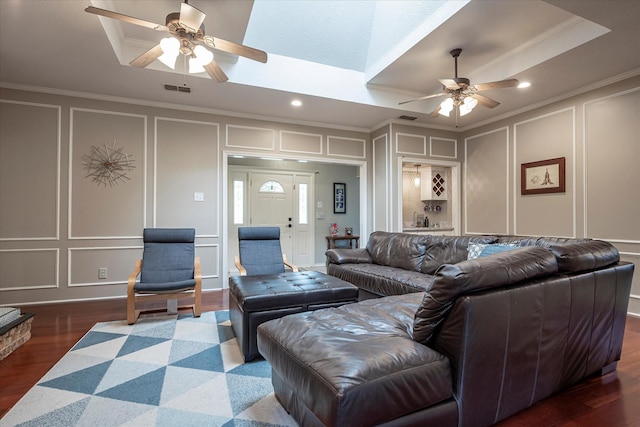 living room featuring dark wood-type flooring, ceiling fan, ornamental molding, and a raised ceiling