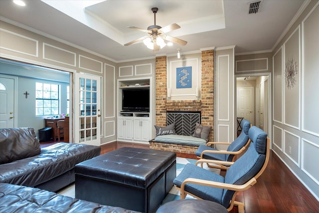 living room with crown molding, dark wood-type flooring, built in features, and a raised ceiling