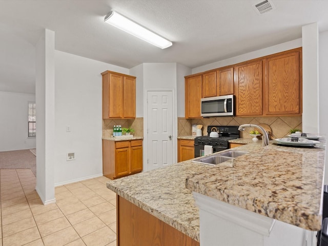 kitchen featuring light tile patterned flooring, visible vents, black range with gas stovetop, brown cabinets, and stainless steel microwave