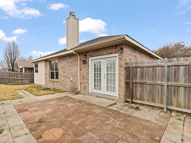 back of house with french doors, brick siding, a chimney, a patio area, and a fenced backyard