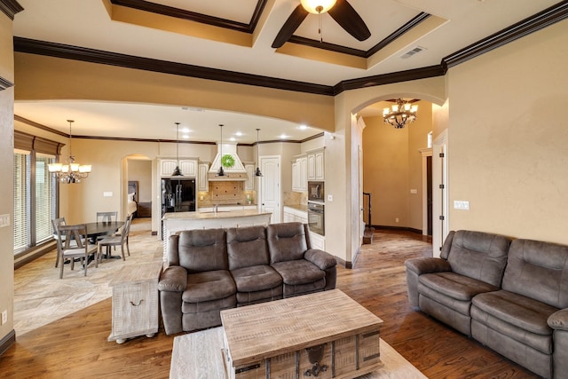 living room featuring hardwood / wood-style flooring, ornamental molding, sink, and ceiling fan with notable chandelier