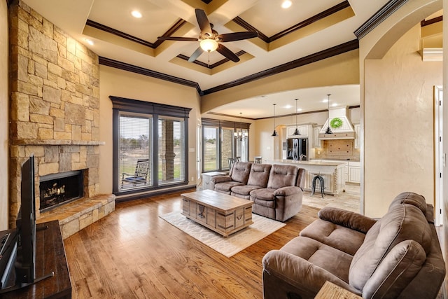 living room with ornamental molding, a stone fireplace, coffered ceiling, and light hardwood / wood-style flooring