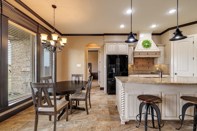 kitchen with premium range hood, decorative light fixtures, black fridge with ice dispenser, and light stone countertops