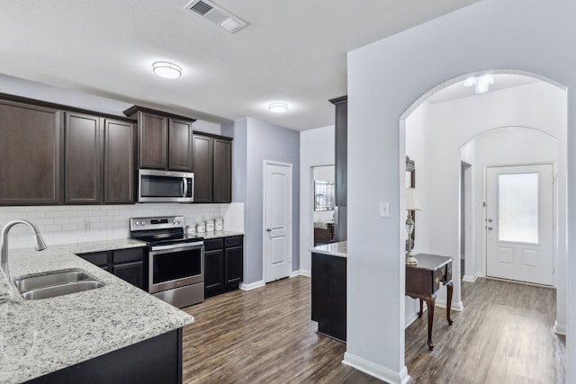 kitchen with sink, appliances with stainless steel finishes, backsplash, light stone counters, and dark hardwood / wood-style flooring