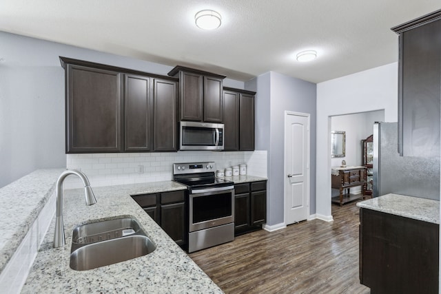 kitchen with dark wood-type flooring, sink, light stone counters, appliances with stainless steel finishes, and backsplash