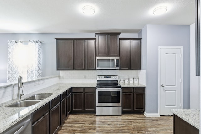 kitchen with dark wood-type flooring, dark brown cabinetry, sink, stainless steel appliances, and backsplash