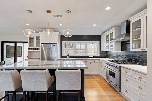 kitchen with sink, premium appliances, pendant lighting, wall chimney range hood, and white cabinets