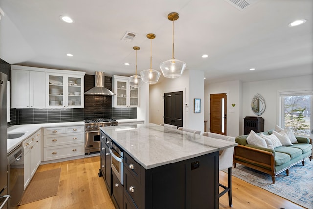 kitchen with wall chimney exhaust hood, a breakfast bar, white cabinetry, hanging light fixtures, and appliances with stainless steel finishes