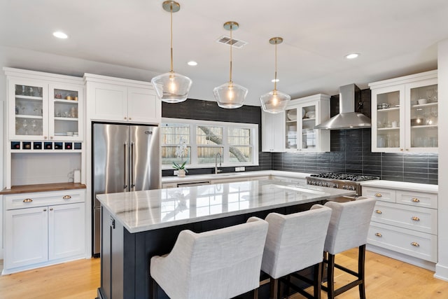 kitchen with a kitchen island, decorative light fixtures, white cabinets, wall chimney range hood, and light wood-type flooring