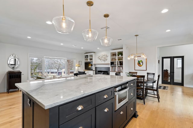 kitchen featuring light stone counters, hanging light fixtures, light hardwood / wood-style flooring, a kitchen island, and oven