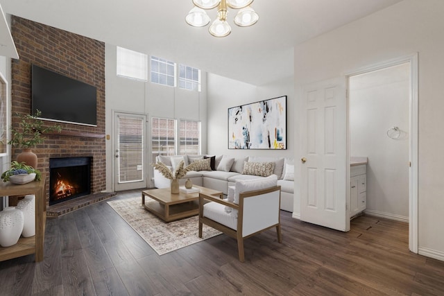 living room featuring a brick fireplace, dark wood-type flooring, and an inviting chandelier