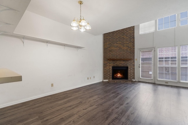 unfurnished living room featuring lofted ceiling, dark hardwood / wood-style floors, a brick fireplace, and a notable chandelier