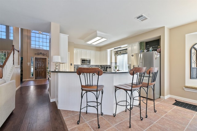 kitchen featuring a breakfast bar area, backsplash, stainless steel appliances, white cabinets, and kitchen peninsula