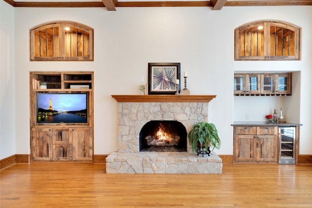 living room with a stone fireplace, hardwood / wood-style floors, wine cooler, ornamental molding, and bar area