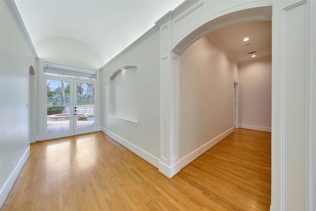 hall with vaulted ceiling, ornamental molding, light hardwood / wood-style floors, and french doors