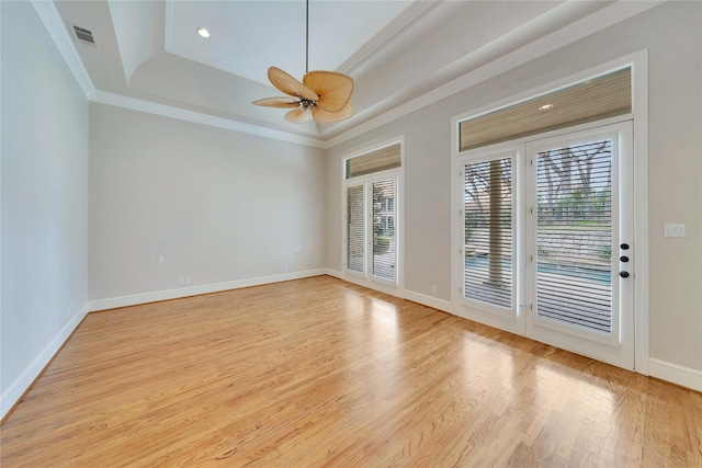 unfurnished room with a tray ceiling, a wealth of natural light, ornamental molding, and light wood-type flooring