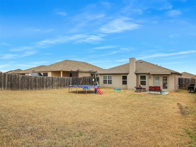 back of house with a trampoline, a yard, and an outdoor fire pit