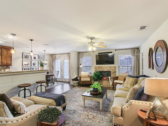 living room with french doors, ceiling fan, wood-type flooring, and a tiled fireplace