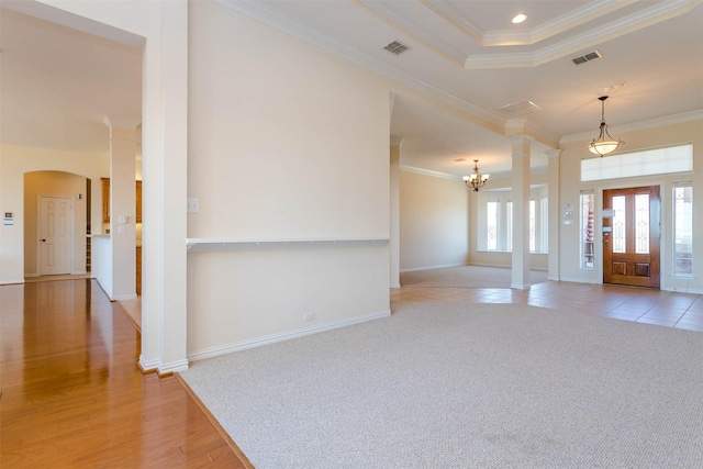 entryway with ornate columns, light colored carpet, a notable chandelier, a tray ceiling, and crown molding