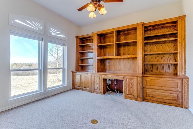 unfurnished office with built in desk, light colored carpet, and ceiling fan