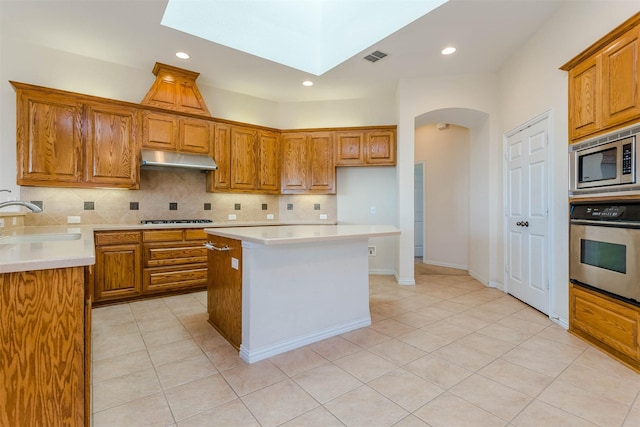 kitchen featuring sink, appliances with stainless steel finishes, a skylight, tasteful backsplash, and a kitchen island