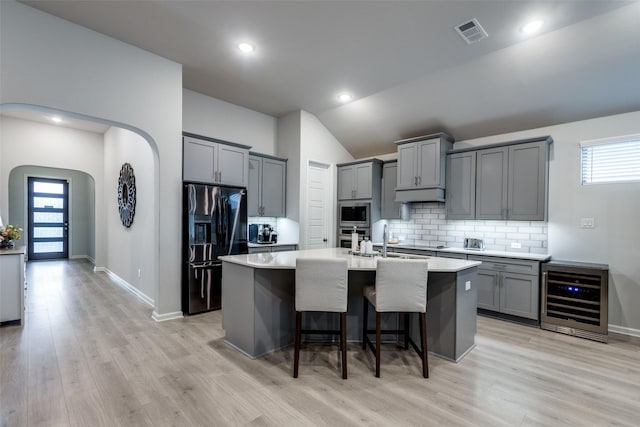 kitchen with sink, a breakfast bar, appliances with stainless steel finishes, an island with sink, and beverage cooler