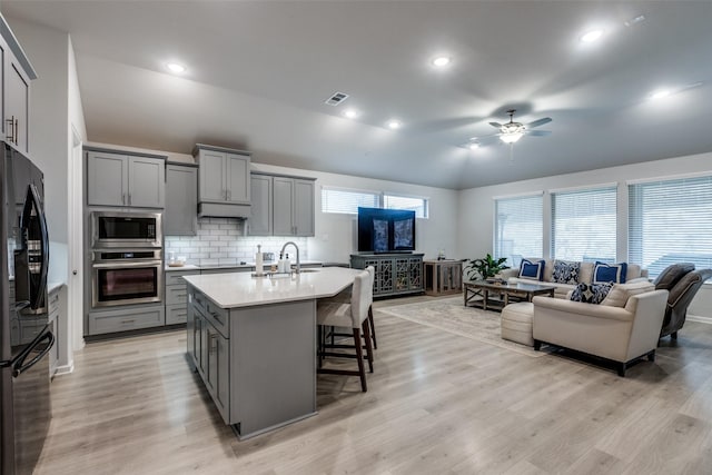 kitchen with a breakfast bar area, stainless steel appliances, gray cabinets, and a center island with sink