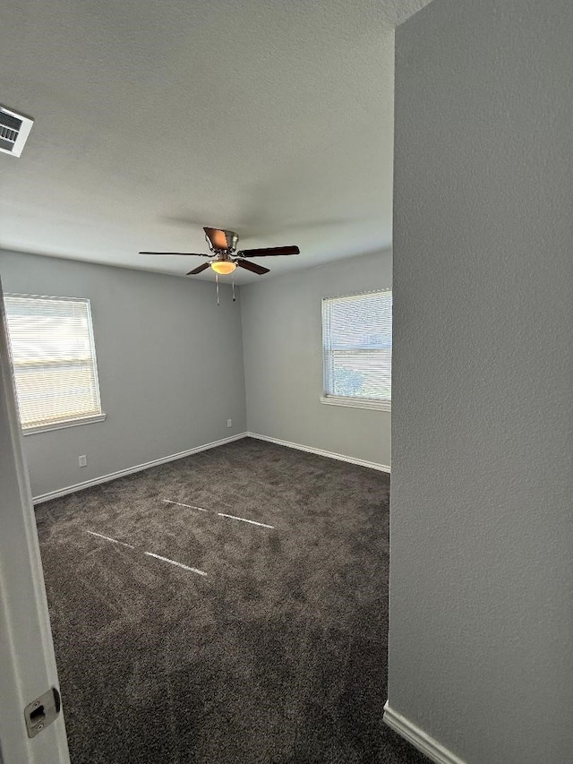 spare room with ceiling fan, a healthy amount of sunlight, a textured ceiling, and dark colored carpet