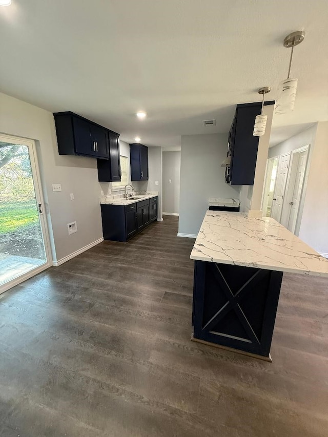 kitchen with sink, hanging light fixtures, kitchen peninsula, light stone countertops, and dark wood-type flooring