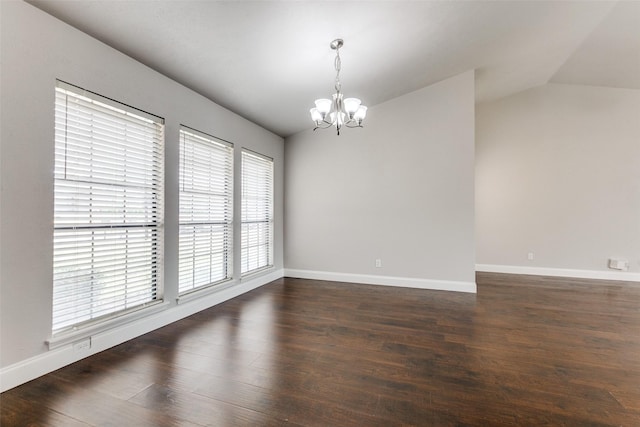 empty room featuring lofted ceiling, dark wood-type flooring, and an inviting chandelier