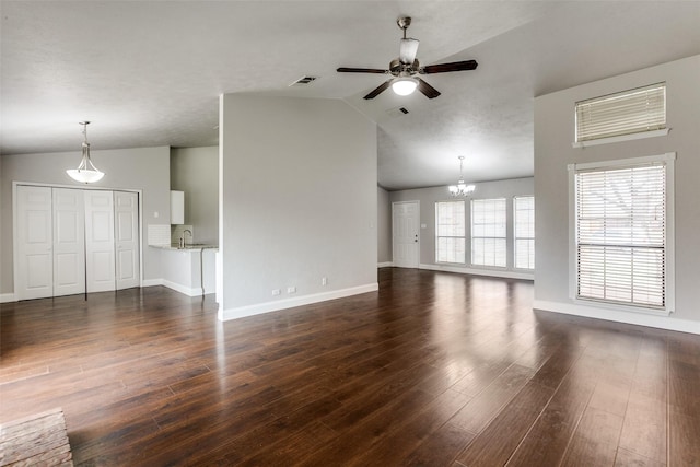 unfurnished living room with ceiling fan with notable chandelier, dark wood-type flooring, and vaulted ceiling