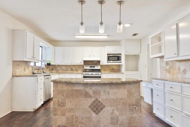 kitchen with stainless steel appliances, white cabinetry, light stone counters, and decorative light fixtures